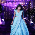 A glamorous Indian woman in a blue lehenga at a vibrant evening event.