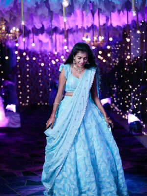 A glamorous Indian woman in a blue lehenga at a vibrant evening event.