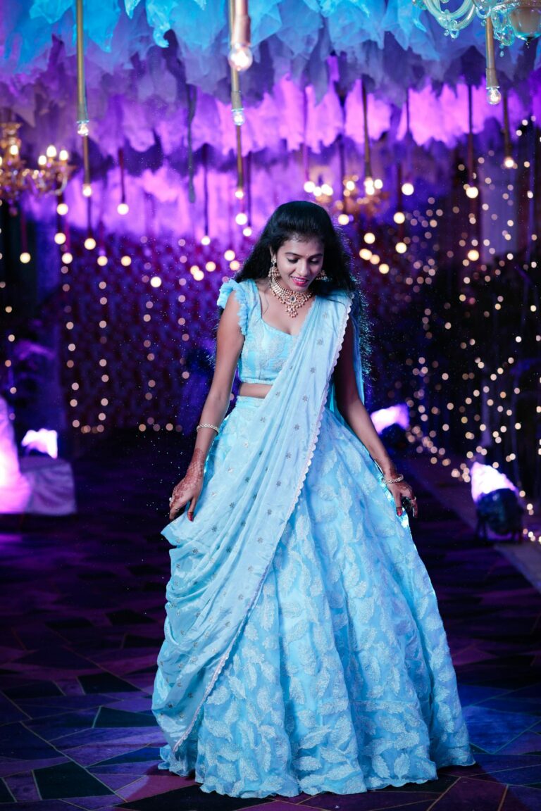 A glamorous Indian woman in a blue lehenga at a vibrant evening event.