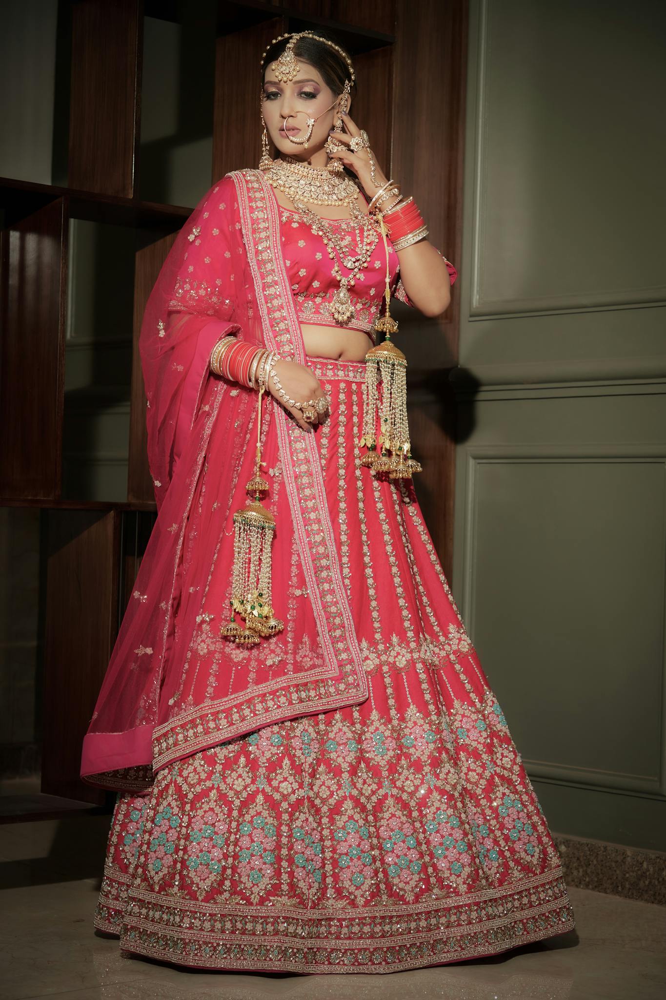 A woman elegantly posing in traditional Indian bridal attire indoors.