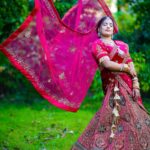 Elegant Indian bride posing outdoors in vibrant traditional wedding outfit.