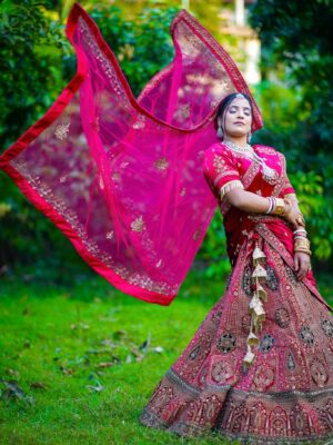 Elegant Indian bride posing outdoors in vibrant traditional wedding outfit.