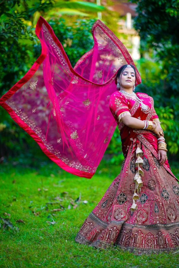 Elegant Indian bride posing outdoors in vibrant traditional wedding outfit.
