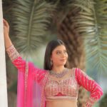 Stunning Indian bridal portrait with palm tree backdrop, wearing a pink lehenga.