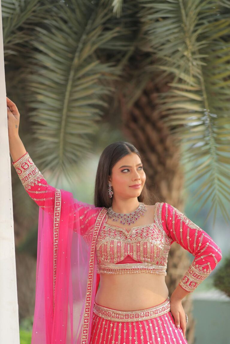 Stunning Indian bridal portrait with palm tree backdrop, wearing a pink lehenga.