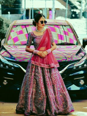 Woman in vibrant Indian lehenga standing in front of a car, showcasing traditional fashion outdoors.