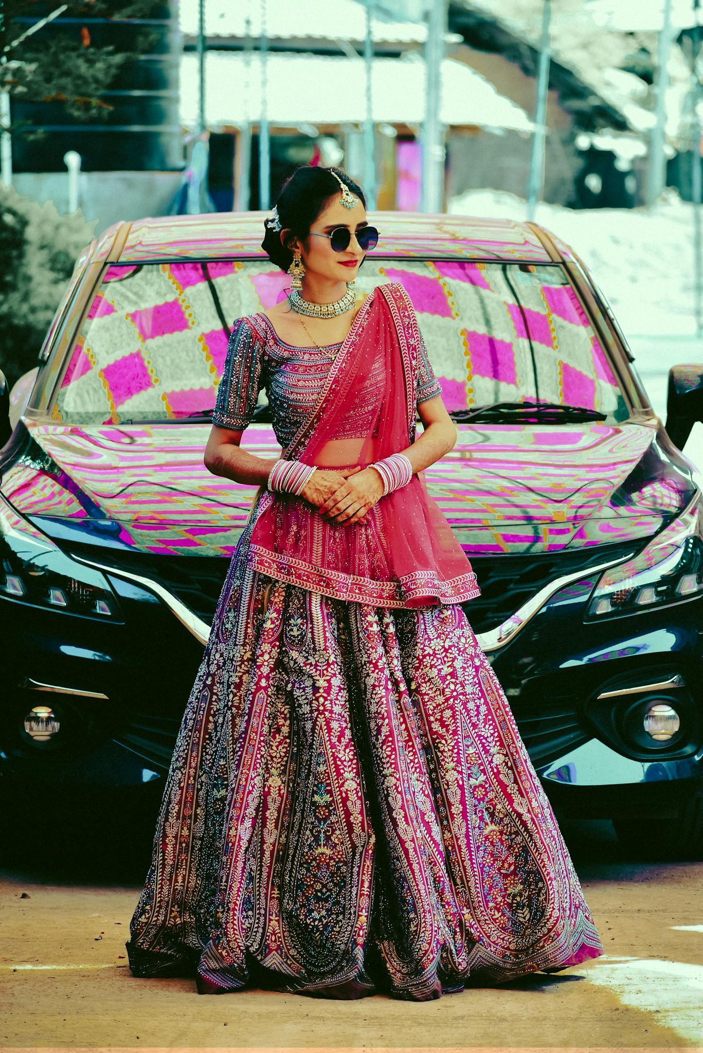 Woman in vibrant Indian lehenga standing in front of a car, showcasing traditional fashion outdoors.